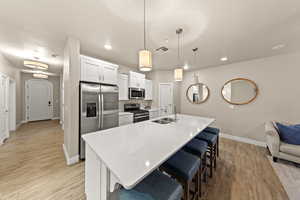 Kitchen with decorative light fixtures, an island with sink, sink, white cabinets, and stainless steel appliances