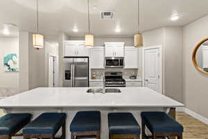 Kitchen with hanging light fixtures, an island with sink, white cabinets, and appliances with stainless steel finishes