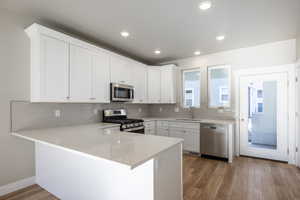 Kitchen with appliances with stainless steel finishes, white cabinetry, sink, backsplash, and kitchen peninsula