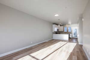 Kitchen with white cabinetry, stainless steel appliances, hanging light fixtures, and light hardwood / wood-style flooring