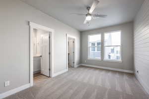 Unfurnished bedroom featuring ensuite bath, a walk in closet, light colored carpet, and ceiling fan