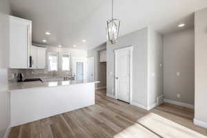 Kitchen with white cabinetry, light hardwood / wood-style flooring, kitchen peninsula, decorative backsplash, and stove