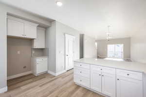 Kitchen featuring tasteful backsplash, white cabinetry, light hardwood / wood-style flooring, and decorative light fixtures