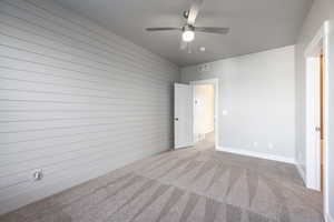 Unfurnished bedroom featuring ceiling fan, light colored carpet, and wood walls