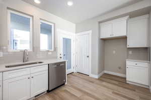 Kitchen featuring sink, white cabinetry, tasteful backsplash, light wood-type flooring, and stainless steel dishwasher