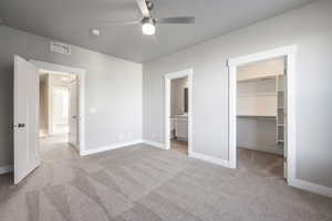 Unfurnished bedroom with ceiling fan, ensuite bathroom, light carpet, a spacious closet, and a closet