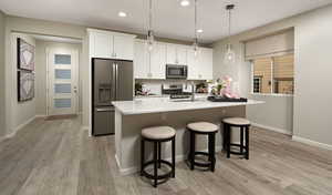 Kitchen with decorative light fixtures, white cabinetry, sink, stainless steel appliances, and a center island with sink