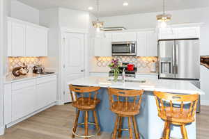 Kitchen featuring pendant lighting, an island with sink, white cabinets, light hardwood / wood-style floors, and stainless steel appliances