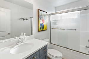 Full bathroom featuring enclosed tub / shower combo, vanity, and toilet