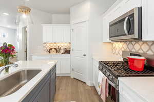 Kitchen featuring sink, decorative light fixtures, appliances with stainless steel finishes, light hardwood / wood-style floors, and white cabinets