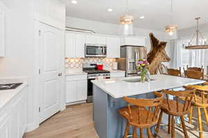 Kitchen with a kitchen island with sink, hanging light fixtures, white cabinets, and appliances with stainless steel finishes