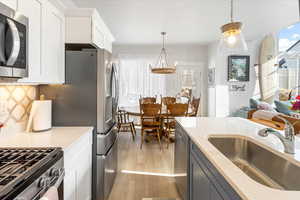 Kitchen with stainless steel appliances, white cabinetry, sink, and pendant lighting