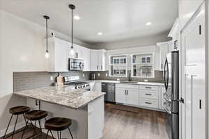 Kitchen featuring appliances with stainless steel finishes, pendant lighting, sink, white cabinets, and kitchen peninsula