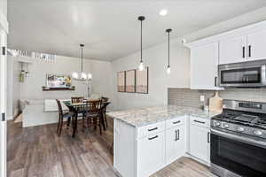 Kitchen featuring appliances with stainless steel finishes, decorative light fixtures, tasteful backsplash, white cabinetry, and kitchen peninsula