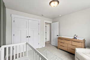 Bedroom featuring a nursery area, light colored carpet, and a closet