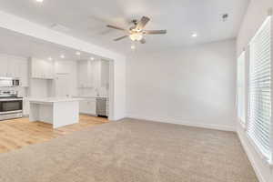 Kitchen featuring white cabinetry, light colored carpet, stainless steel appliances, and a center island