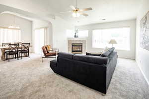 Living room featuring a tiled fireplace, vaulted ceiling, and light colored carpet