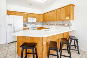 Kitchen with a breakfast bar, sink, backsplash, kitchen peninsula, and white appliances