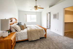 Bedroom with carpet floors, a walk in closet, ceiling fan, and vaulted ceiling