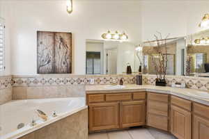 Bathroom featuring tile patterned flooring, vanity, a relaxing tiled tub, and backsplash