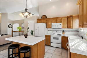 Kitchen with pendant lighting, sink, white appliances, light tile patterned floors, and a kitchen island