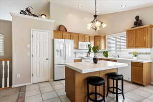 Kitchen featuring pendant lighting, light tile patterned floors, white appliances, a center island, and tile counters