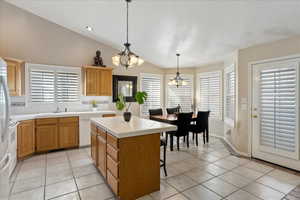 Kitchen with pendant lighting, dishwasher, an inviting chandelier, a center island, and vaulted ceiling