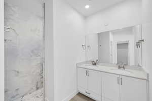 Bathroom featuring double vanity, baseboards, walk in shower, and a sink