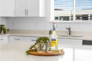 Kitchen featuring white cabinets, dishwashing machine, light countertops, and a sink