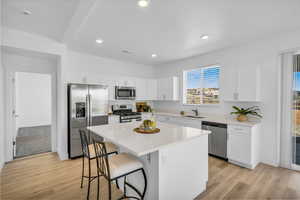 Kitchen featuring a center island, light countertops, appliances with stainless steel finishes, white cabinets, and a sink