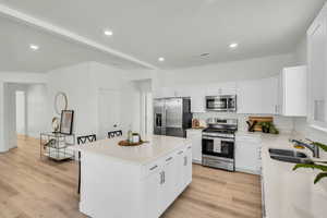 Kitchen with a sink, white cabinets, light countertops, appliances with stainless steel finishes, and a center island