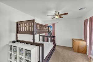 Bedroom with light carpet, ceiling fan, and a textured ceiling