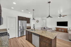 Kitchen with pendant lighting, sink, stainless steel appliances, light stone counters, and a center island with sink