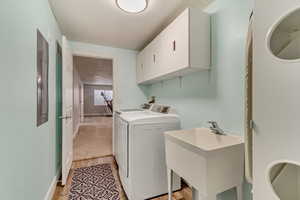 Laundry area featuring washer and dryer, sink, cabinets, and light hardwood / wood-style floors.