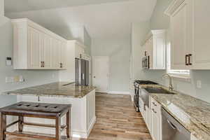 Kitchen with a kitchen bar, white cabinetry, light stone counters, kitchen peninsula, and stainless steel appliances.