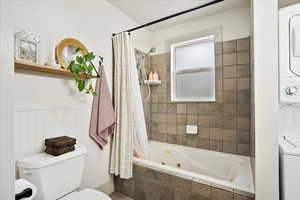 Bathroom with stacked washer / dryer, toilet, and shower / tub combo