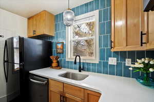 Kitchen featuring black refrigerator, pendant lighting, tasteful backsplash, dishwasher, and sink