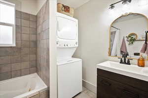 Bathroom featuring stacked washing maching and dryer, vanity, and tiled shower / bath