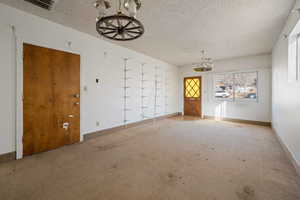 Unfurnished room featuring carpet floors, a textured ceiling, and a chandelier