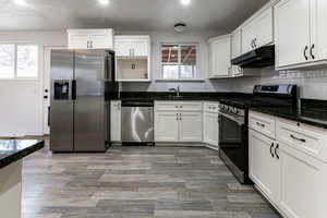 Kitchen with dark stone countertops, backsplash, white cabinets, and appliances with stainless steel finishes