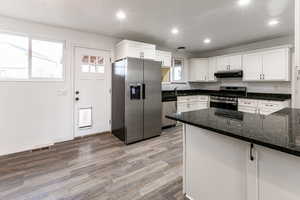 Kitchen featuring appliances with stainless steel finishes, hardwood / wood-style floors, tasteful backsplash, white cabinets, and dark stone counters