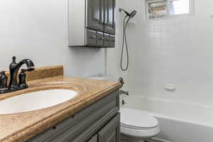 Full bathroom with vanity, tiled shower / bath combo, and toilet