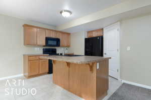 Kitchen with sink, a breakfast bar area, a kitchen island with sink, black appliances, and light tile patterned flooring