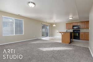 Kitchen featuring hanging light fixtures, a kitchen breakfast bar, black appliances, an island with sink, and light colored carpet