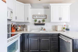 Bar featuring white cabinetry, sink, white appliances, and backsplash