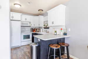 Kitchen with white appliances, kitchen peninsula, sink, and white cabinets