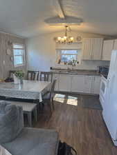 Kitchen with white cabinetry, sink, hanging light fixtures, a notable chandelier, and dark wood-type flooring