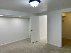 Basement with light colored carpet and a textured ceiling