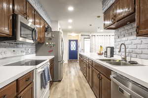 Kitchen featuring pendant lighting, sink, backsplash, stainless steel appliances, and light hardwood / wood-style floors