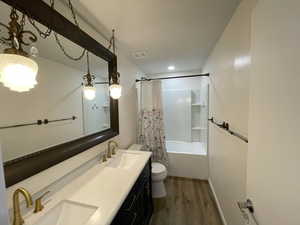 Full bathroom with hardwood / wood-style flooring, shower / tub combo with curtain, vanity, and toilet